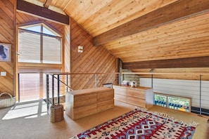 A high-ceilinged room with wooden beams, a built-in bench, a small table, and a patterned rug.