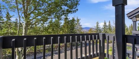 A wooden deck with a railing overlooking a road and trees.