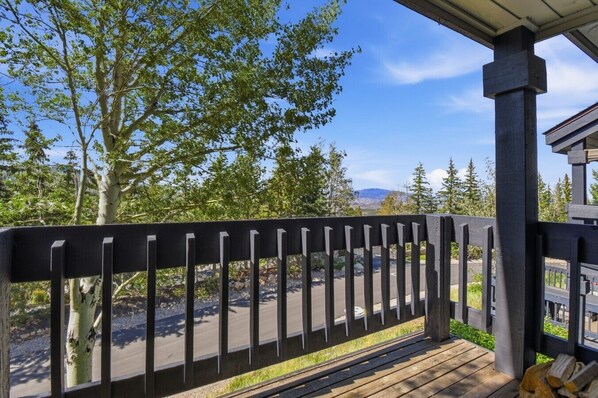 A wooden deck with a railing overlooking a road and trees.