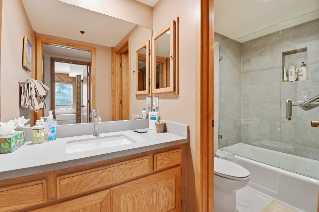 A modern bathroom with a large mirror, wooden cabinetry, a white sink, and a glass-enclosed shower area.