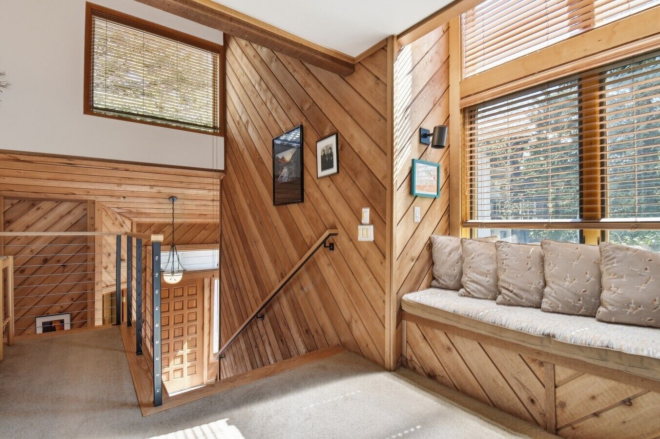 Interior de madera con una escalera, un banco y cuadros en las paredes.