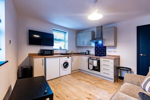 A compact kitchen with a washing machine, oven, microwave, and a TV. - Harcourt 1D: 2BR Flat with Parking in Newark (Newark-on-Trent)