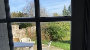 Blick durch ein Fenster auf eine Steinsäule, einen weißen Plastiktisch und Stühle draußen.