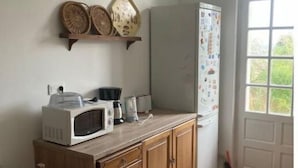Eine Küche mit Mikrowelle, Toaster und Kühlschrank. Es gibt einen Holzkästen und ein Fenster mit Blick ins Grüne.