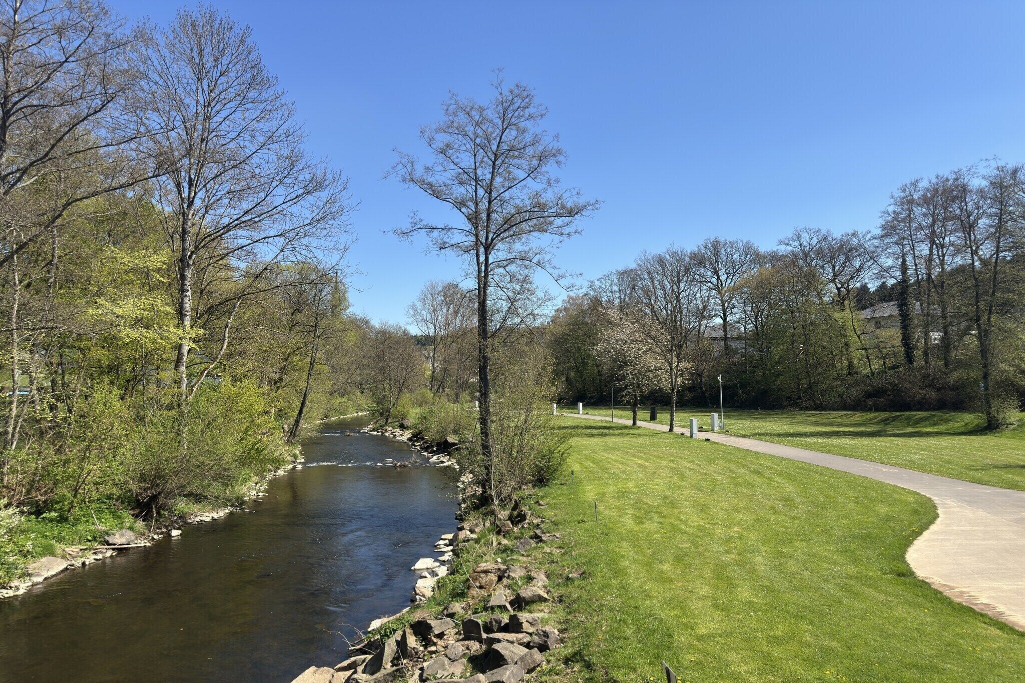 A river with a stone border, a grassy area, and trees.