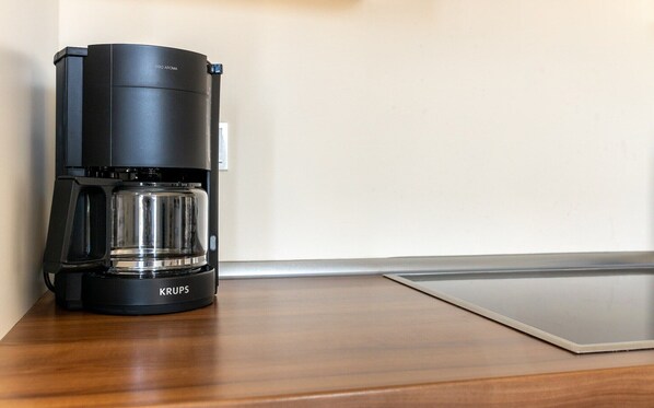 A black coffee maker with a glass carafe on a wooden table against a wall.