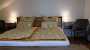 A bedroom with a wooden bed, patterned bedding, two bedside lamps, and a chair. - Moderne Ferienwohnung mit Atemberaubender Aussicht bei Heidelberg (Dossenheim)
