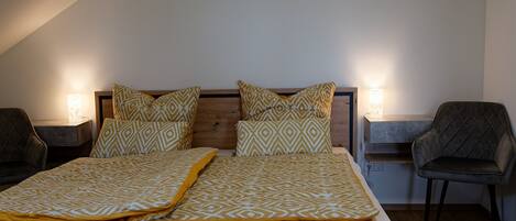 A bedroom with a wooden bed, patterned bedding, two bedside lamps, and a chair.