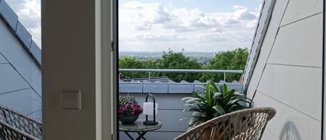 A balcony with wicker chairs, a small table with a potted plant, and a view of the cityscape.