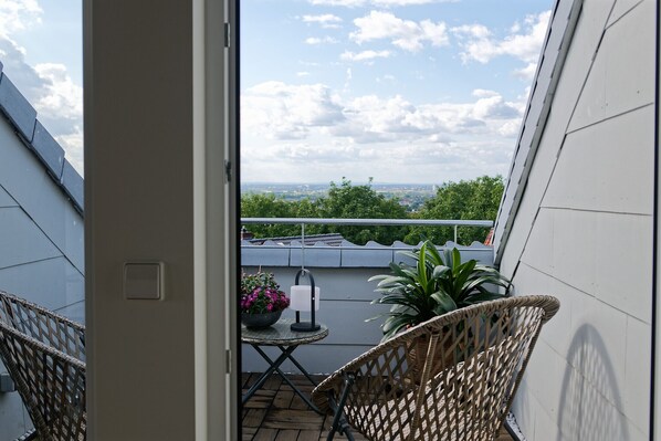 A balcony with wicker chairs, a small table with a potted plant, and a view of the cityscape. - Moderne Ferienwohnung mit Atemberaubender Aussicht bei Heidelberg (Dossenheim)