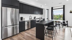 A modern kitchen with a stainless steel refrigerator, black cabinets, and a central island with bar stools.