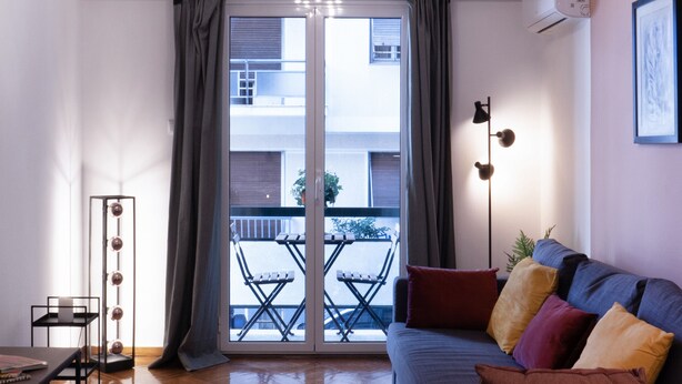 A modern living room with a sofa, a floor lamp, and a view through a glass door to an outdoor balcony. - Modern 1BR Apt, Next to Goulandris (Athens)