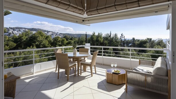 Een balkon met een tafel, stoelen, een bank en een kleine tafel met een glas wijn en een bord eten.