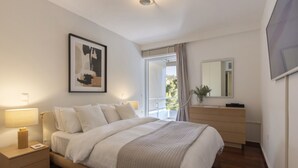 Een slaapkamer met een bed, nachtkastje, lamp en een ingelijst schilderij aan de muur.