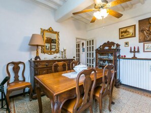 Un comedor con una mesa y sillas de madera, un ventilador de techo, un espejo y un armario con puertas de vidrio.