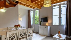 A dining area with a table set for four, a television on a cabinet, and a window with curtains. - Château De Kergonano, dans l'Orangerie by Interhome (Baden)