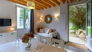 A modern room with a wooden ceiling, a bed with white bedding, a TV on a white cabinet, and a dining table with wine glasses and a vase of flowers. - Château De Kergonano, dans l'Orangerie by Interhome (Baden)