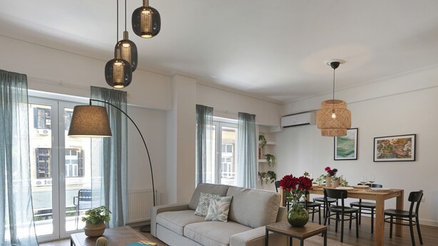 En moderne stue med sofa, sofabord, spisebord og stole. Der er planter, en vase med blomster og billeder på væggene.