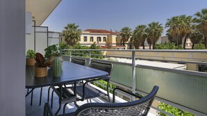 En balkon med bord og stole, med udsigt over et boligområde med palmer og en bygning med rødt tag.
