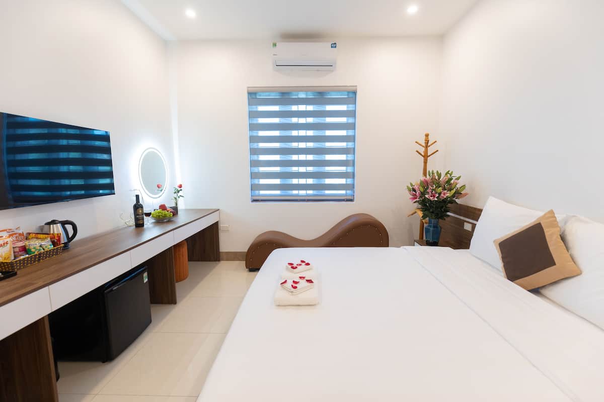 A modern hotel room with a bed, bedside table, TV, and a small desk area.