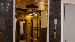 A luxurious entrance with a marble floor, a golden elevator, and a red carpet leading to a room. - Royal Hotel - Sai Dong - Long Biên (Hanoi)