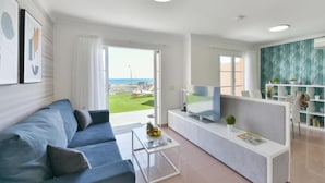 Una sala de estar moderna con un sofá azul, una mesa de centro, un televisor de pantalla plana y vista al mar.
