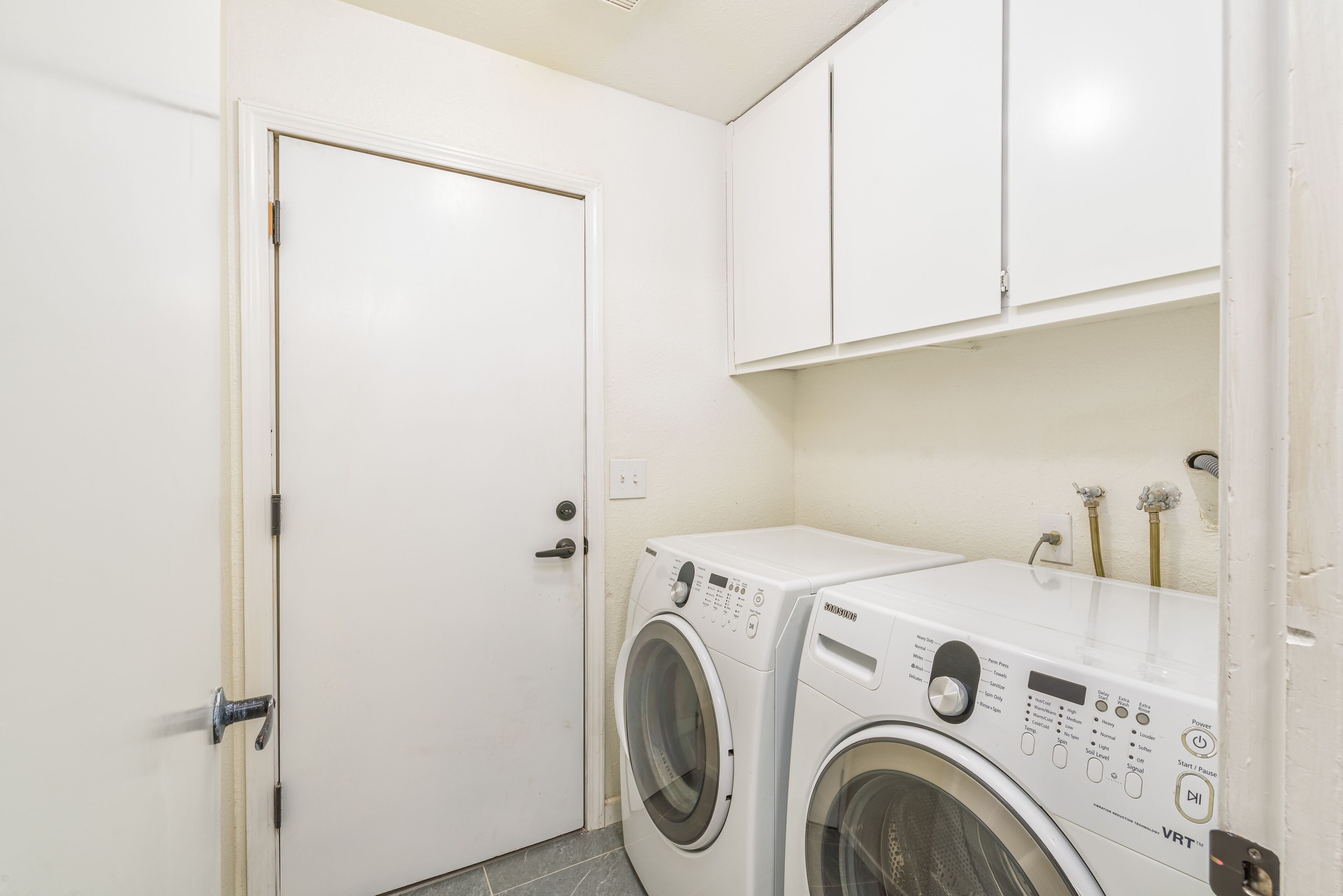 Un cuarto de lavandería con lavadora y secadora, armarios blancos y una puerta.
