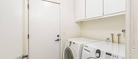 Un cuarto de lavandería con lavadora y secadora, armarios blancos y una puerta.