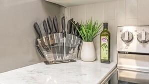 Een keukenblad met een messenblok, een bloempot en een fles olijfolie.