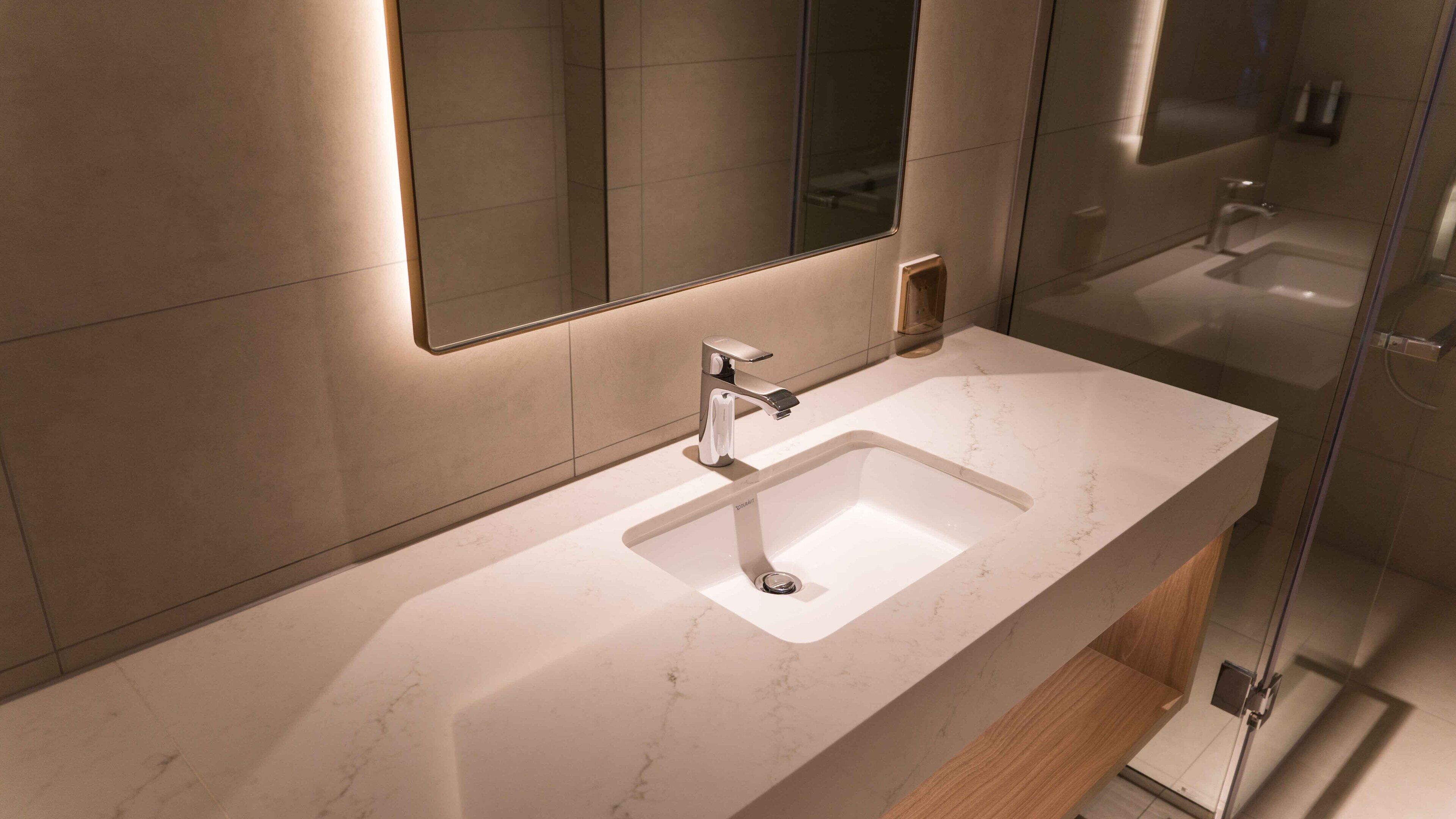 A modern bathroom with a large mirror, a sink, and a shower area.