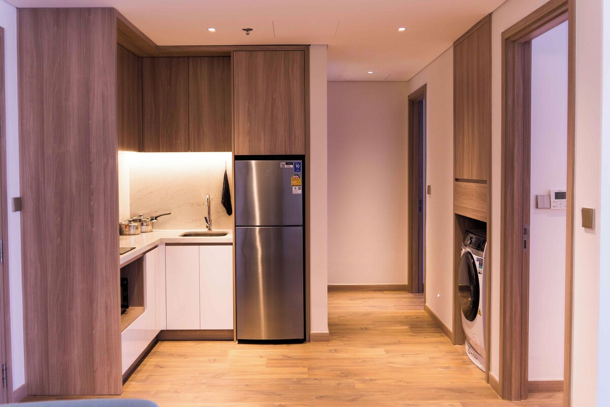 A modern kitchen with a stainless steel refrigerator, a sink, and wooden cabinets.