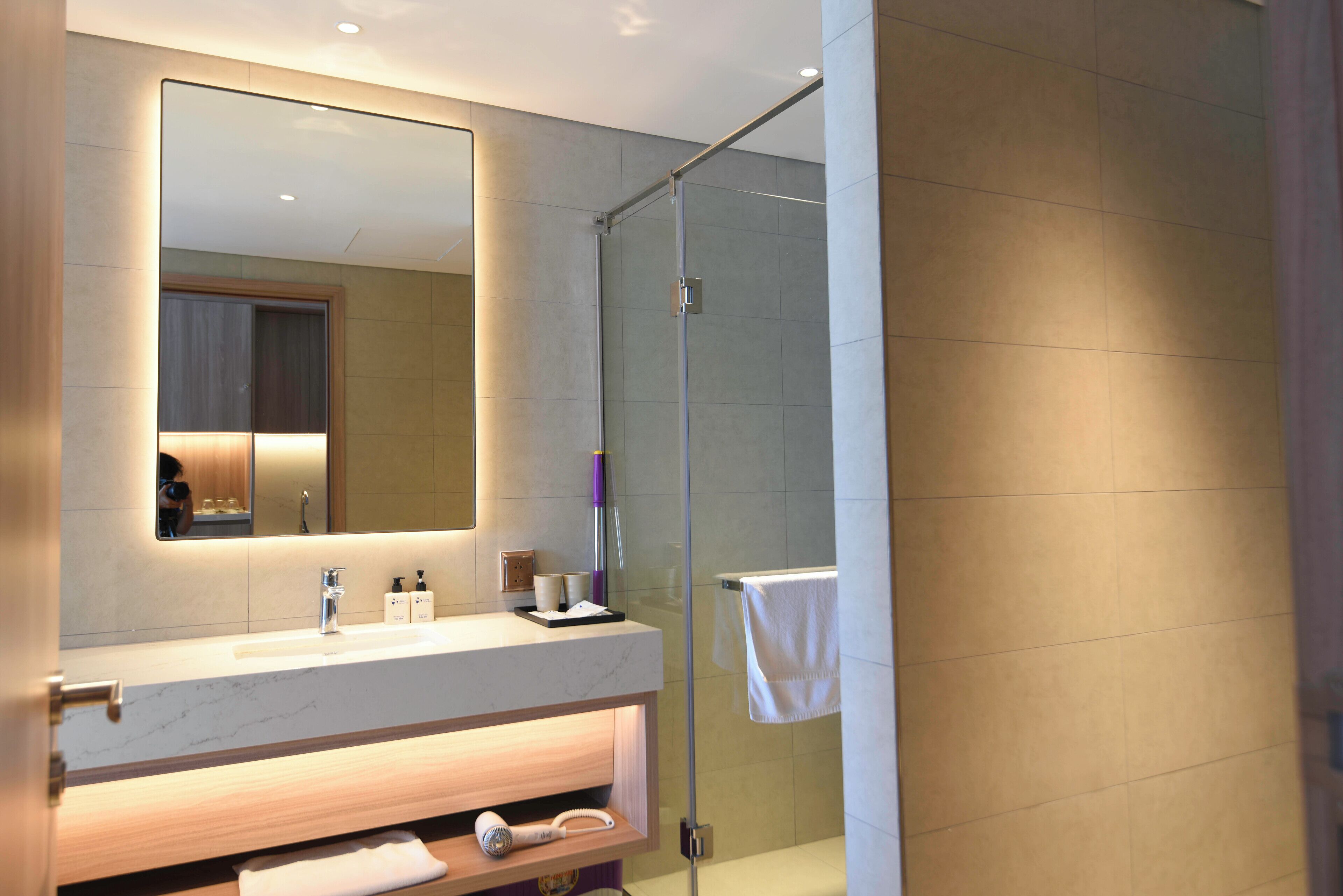 A modern bathroom with a marble sink, a large mirror, a glass shower enclosure, and a towel hanging on the wall.