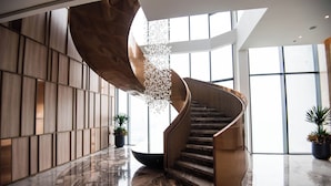 A spiral staircase with a wooden finish, surrounded by a polished marble floor and large windows. - Anstay Residence by A La Carte Hạ Long (Bai Chay)