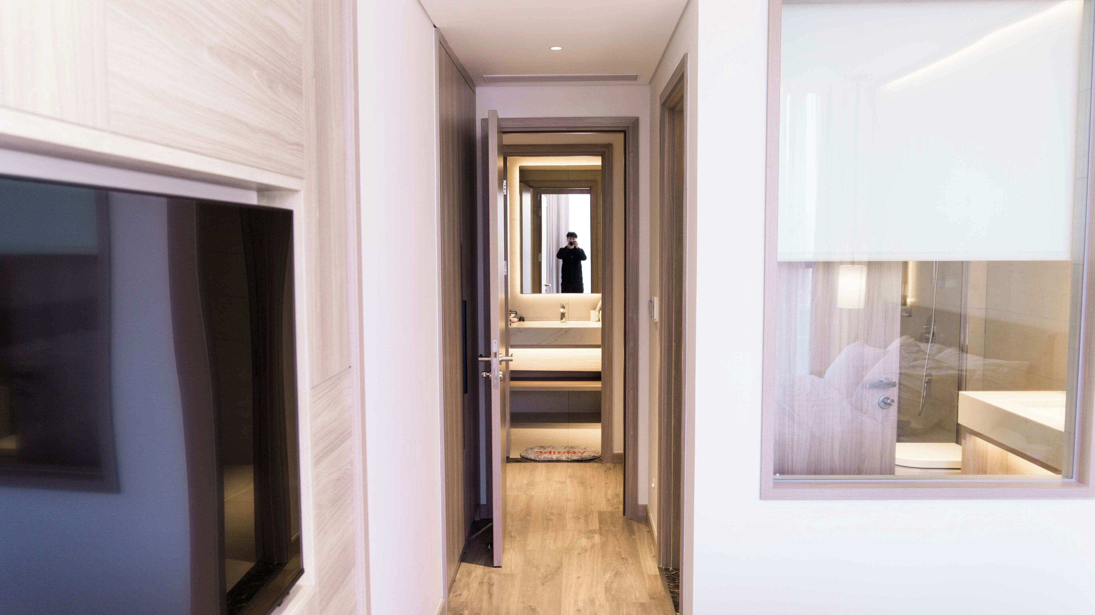 A hallway leading to a bathroom with a shower, a toilet, and a sink.