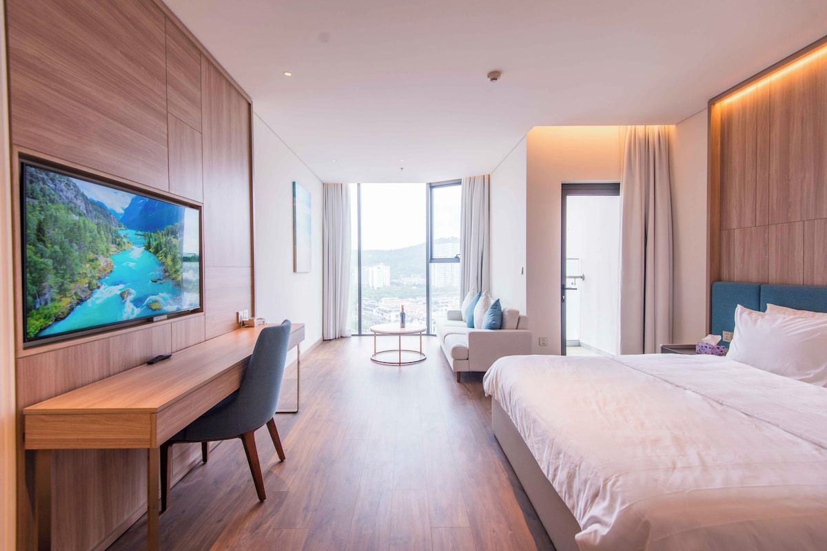 Et moderne hotelværelse med et stort fjernsyn, et skrivebord, en behagelig sofa, en seng og udsigt over byen.