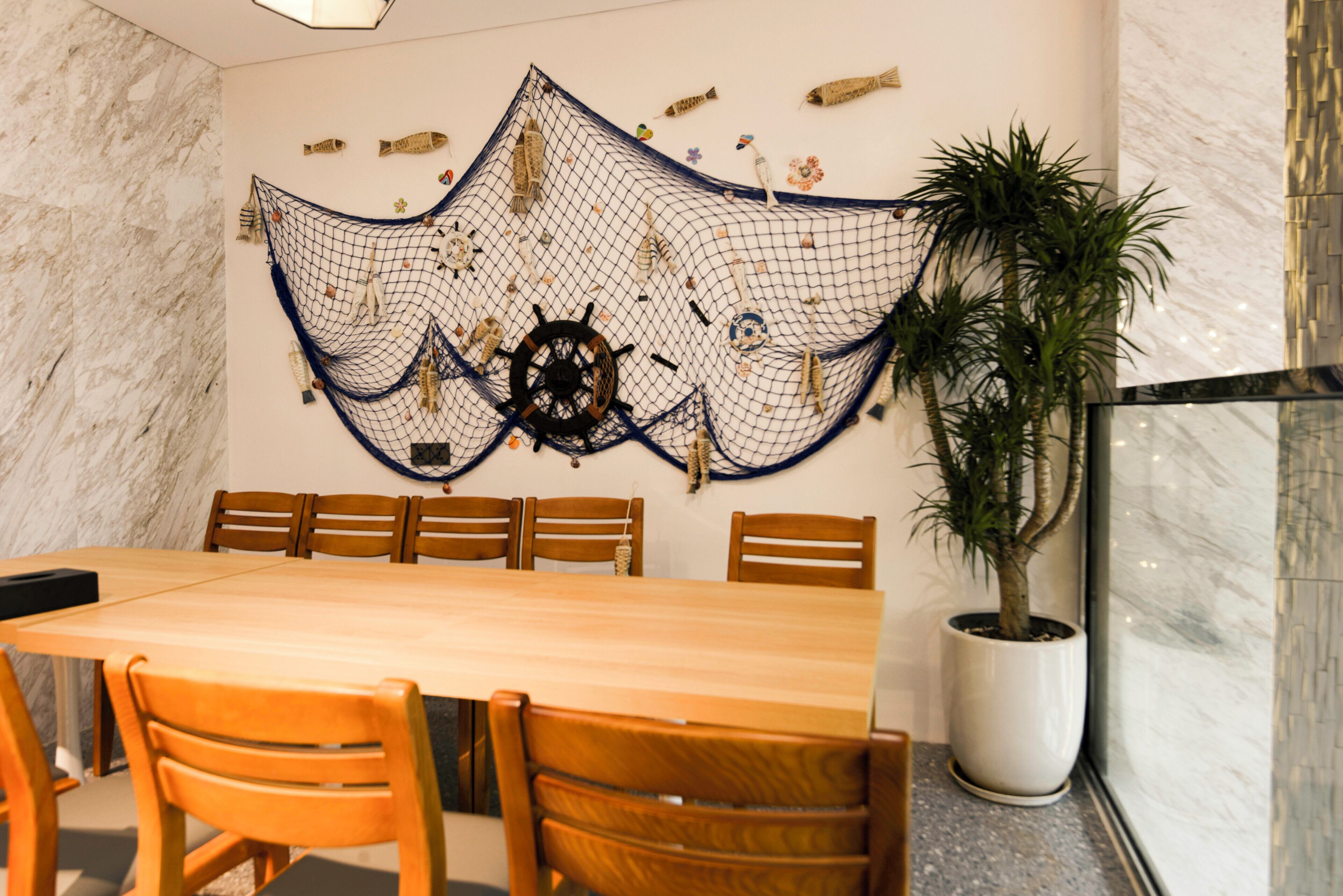 A dining area with a wooden table and chairs, a decorative wall hanging, and a potted plant.