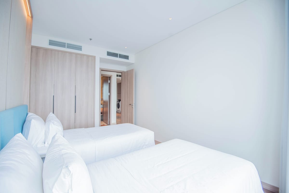 A modern hotel room with two beds, a wardrobe, and a bathroom visible through an open door.