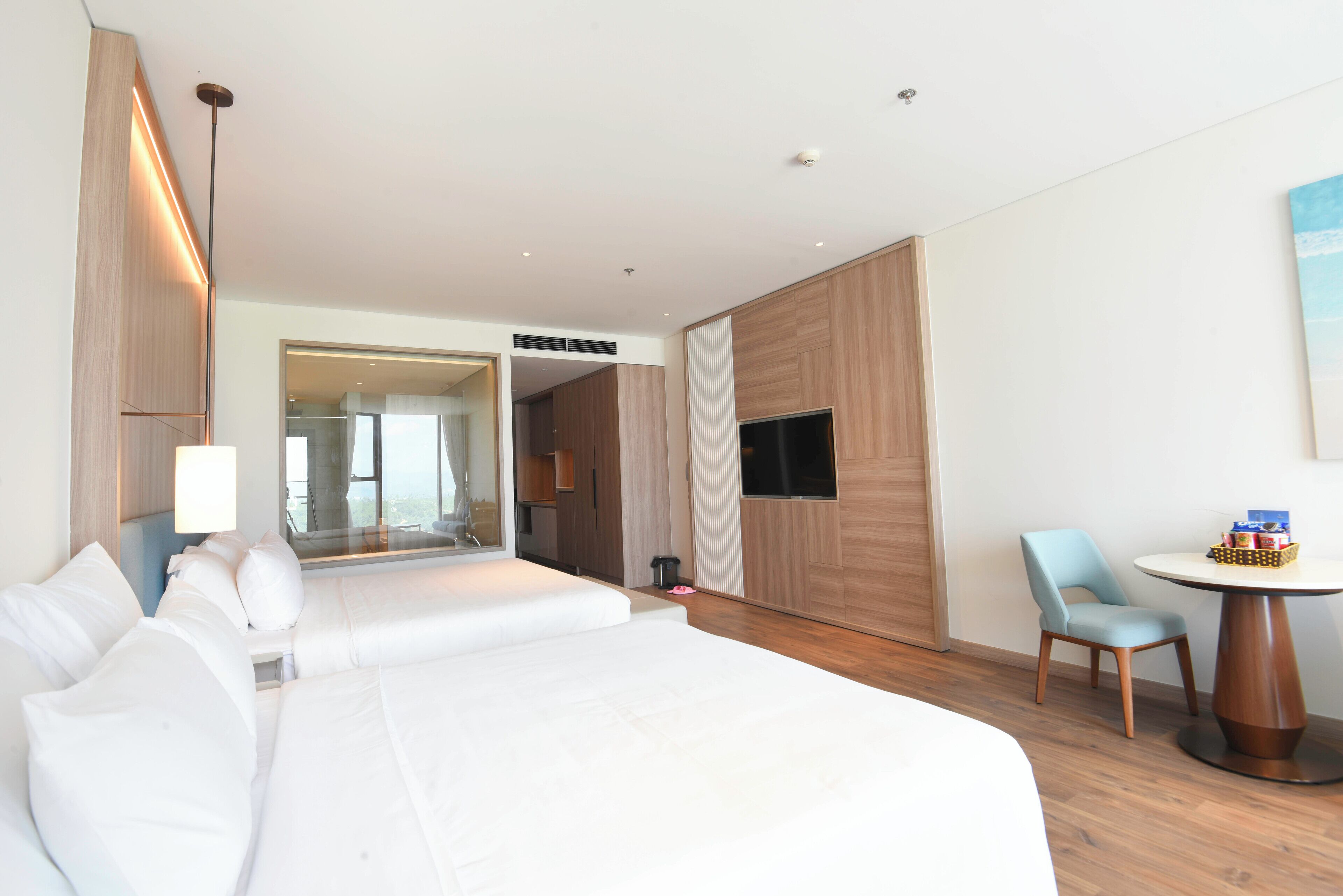 A hotel room with two beds, a TV, a dining table, and a view of the city.