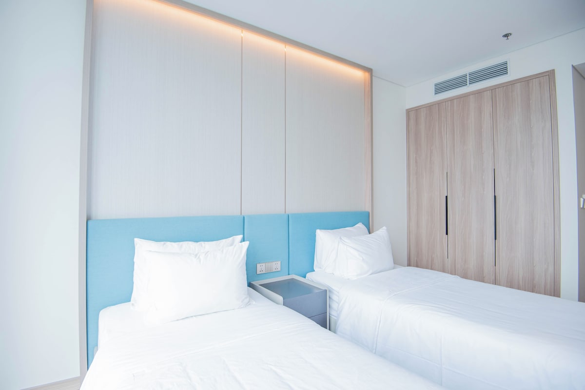 A hotel room with two beds, a wardrobe, and a bedside table.
