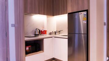A compact kitchen with a stainless steel refrigerator, a microwave, a kettle, and a coffee maker.
