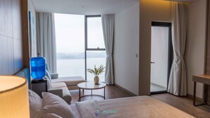 Ein modernes Hotelzimmer mit einem großen Bett, einem Sofa, einem kleinen Tisch und Meerblick durch ein großes Fenster.