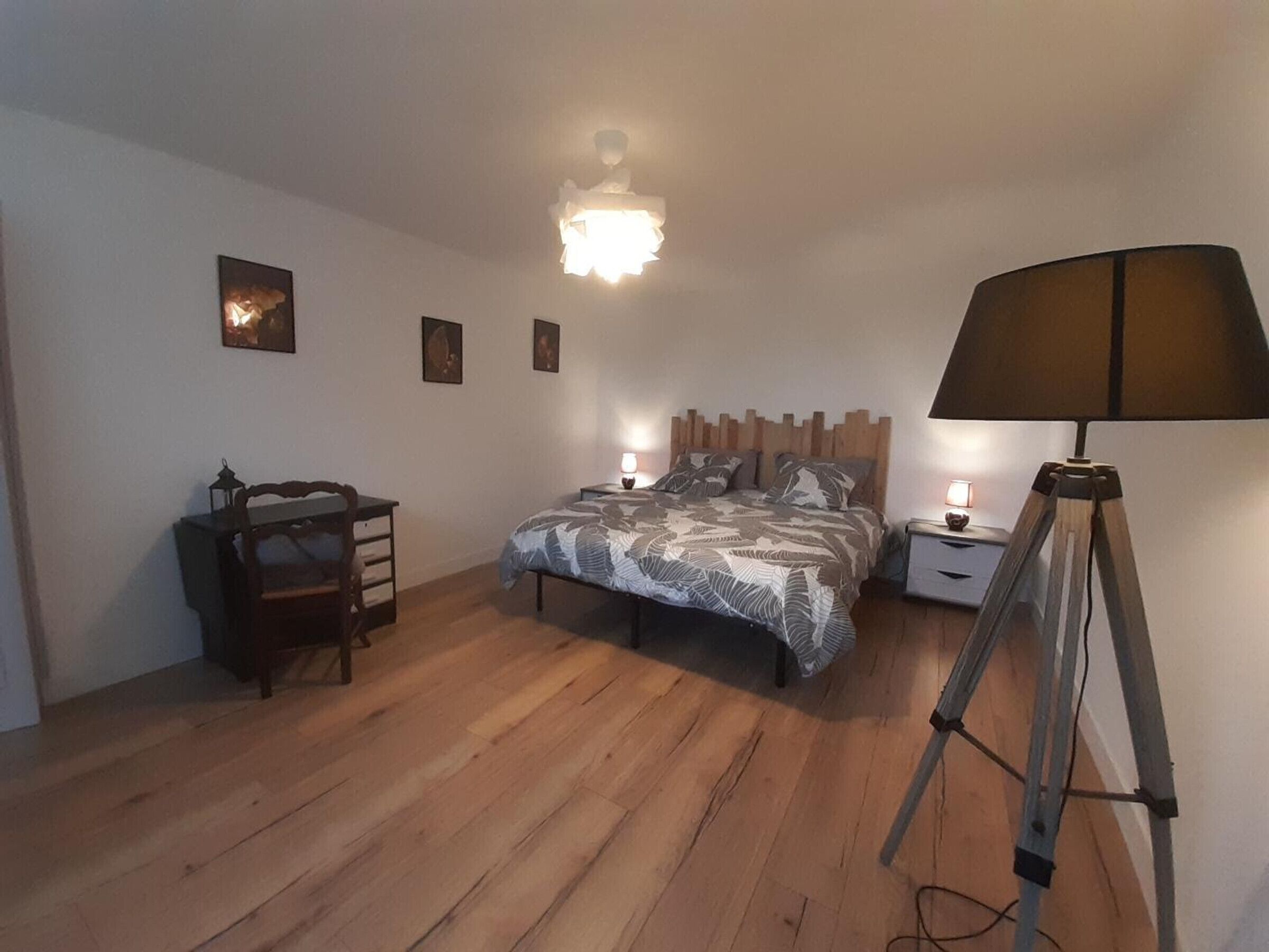 Ein Schlafzimmer mit Holzboden, einem Bett mit gemusterten Textilien, einem Schreibtisch mit Stuhl, zwei Nachttischen mit Lampen sowie einer Stehlampe.