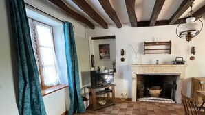 A cozy living room with a fireplace, wooden beams, a television, and a dining area.