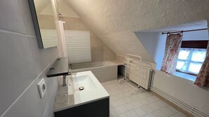 A modern bathroom with a bathtub, a sink, and a window with curtains.