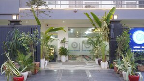 The entrance of a hotel with a modern design, featuring a glass facade, potted plants, and a signboard with the hotel's name. - Posh Garden Inn (Gurugram)