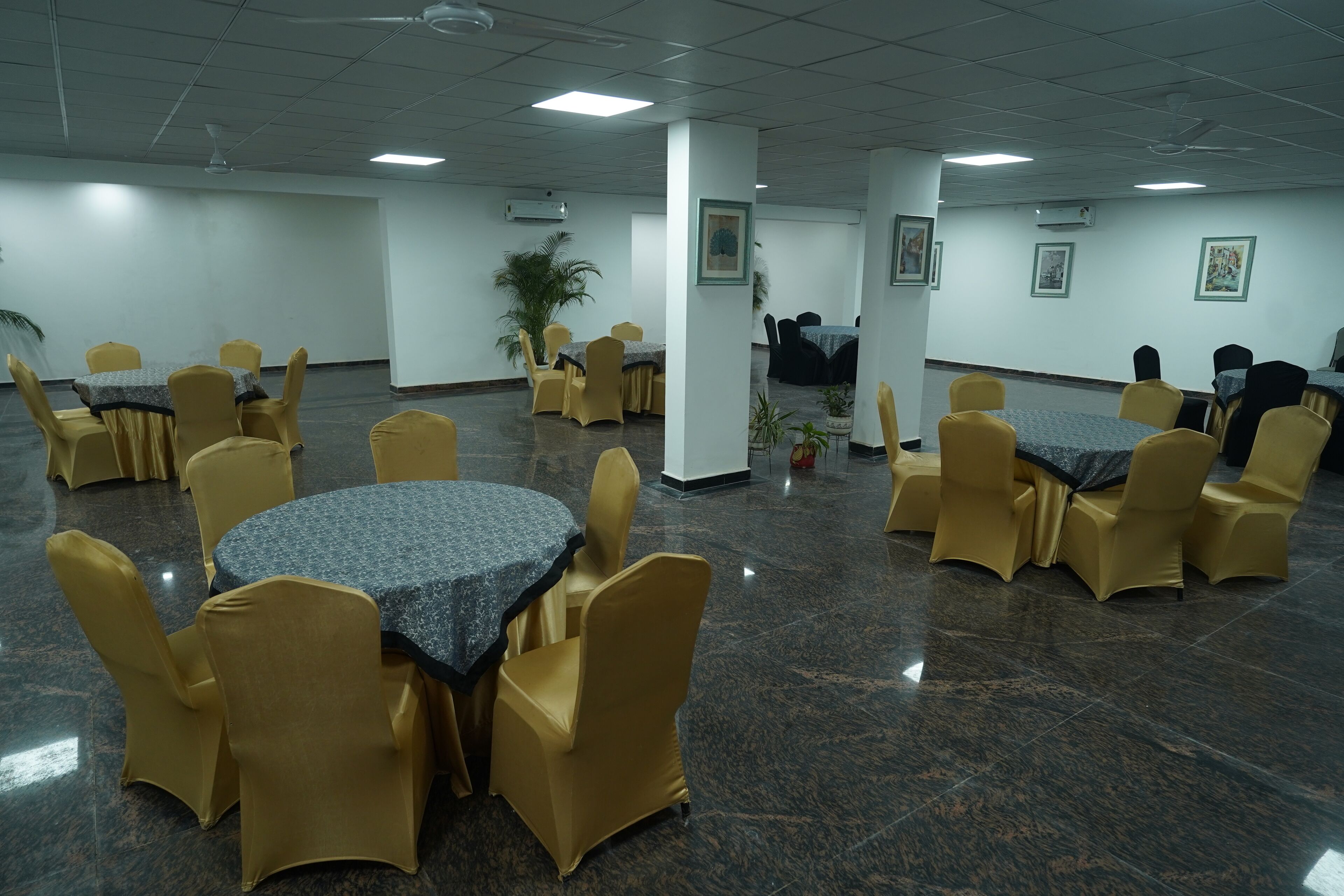 A conference room with round tables and yellow chairs, air conditioning units, and framed artwork on the walls.