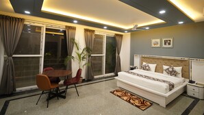 A modern bedroom with a bed, bedside table, and a dining area with a table and chairs. - Posh Garden Inn (Gurugram)