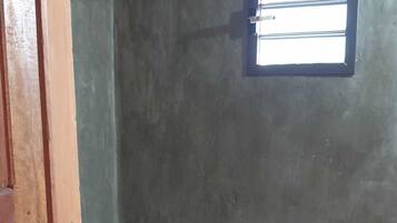Een badkamer met een betonnen muur, een klein raam, een toilet en een douche.
