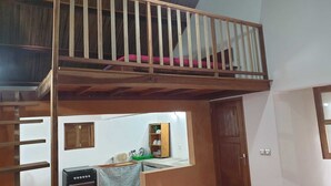 Una habitación con cama elevada, una zona de cocina con estufa y una puerta de madera.
