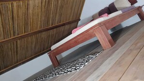 Un banco de madera con cojines, un muro de fondo, un tapete estampado en el suelo y un aparador de madera.